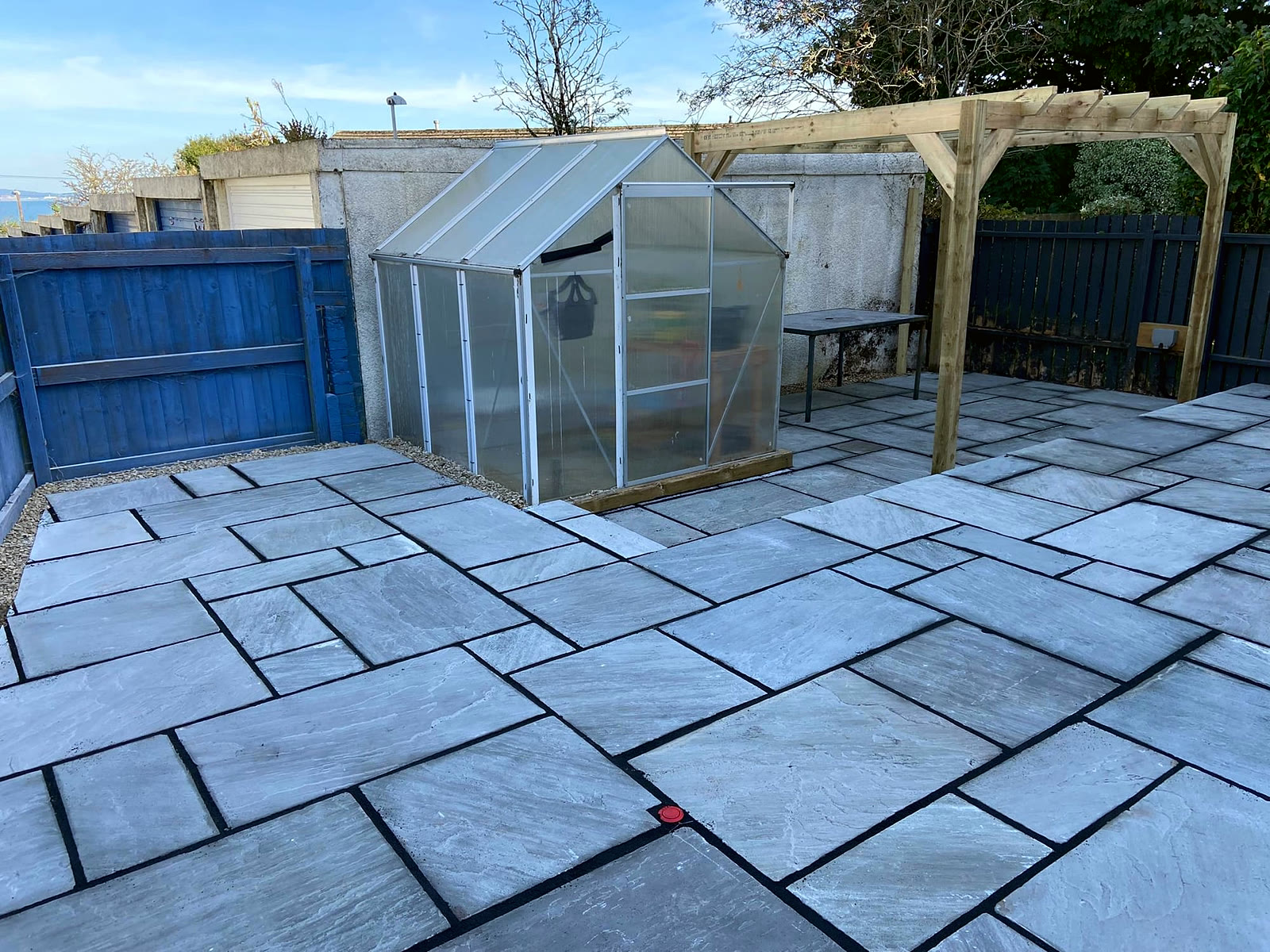 Grey Indian sandstone patio laid around a greenhouse