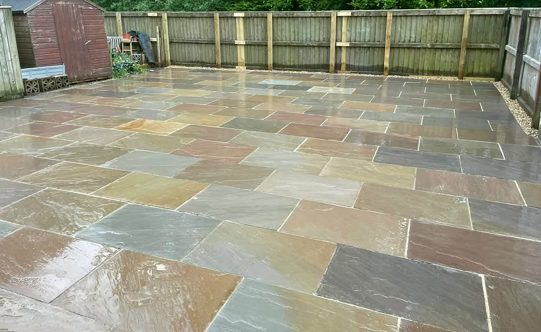 A freshly laid Indian sandstone patio in buff, grey and rust tones, wet after rain